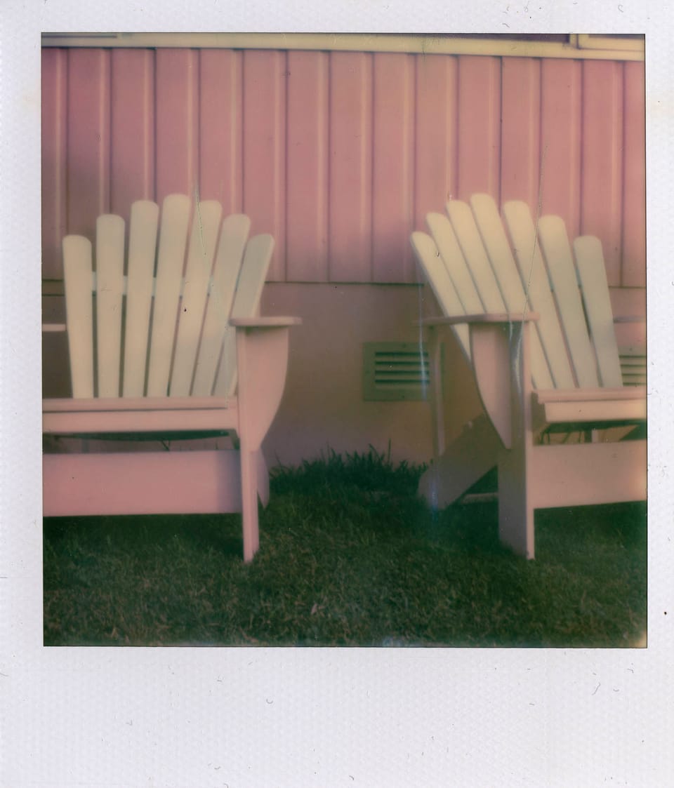 photograph of pink weatherboard on the side of a house with two pink and white adirondack-style chairs on the grass in front